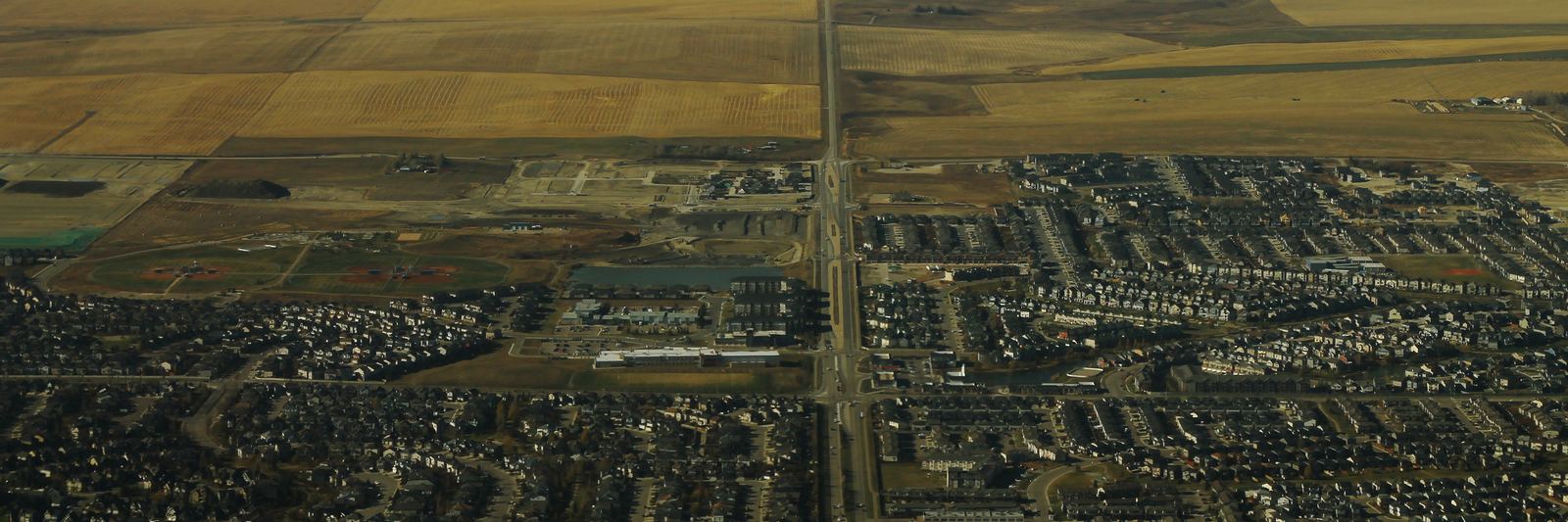 Aerial view of Airdrie, Alberta, looking west over residential streets and a main road toward farmland