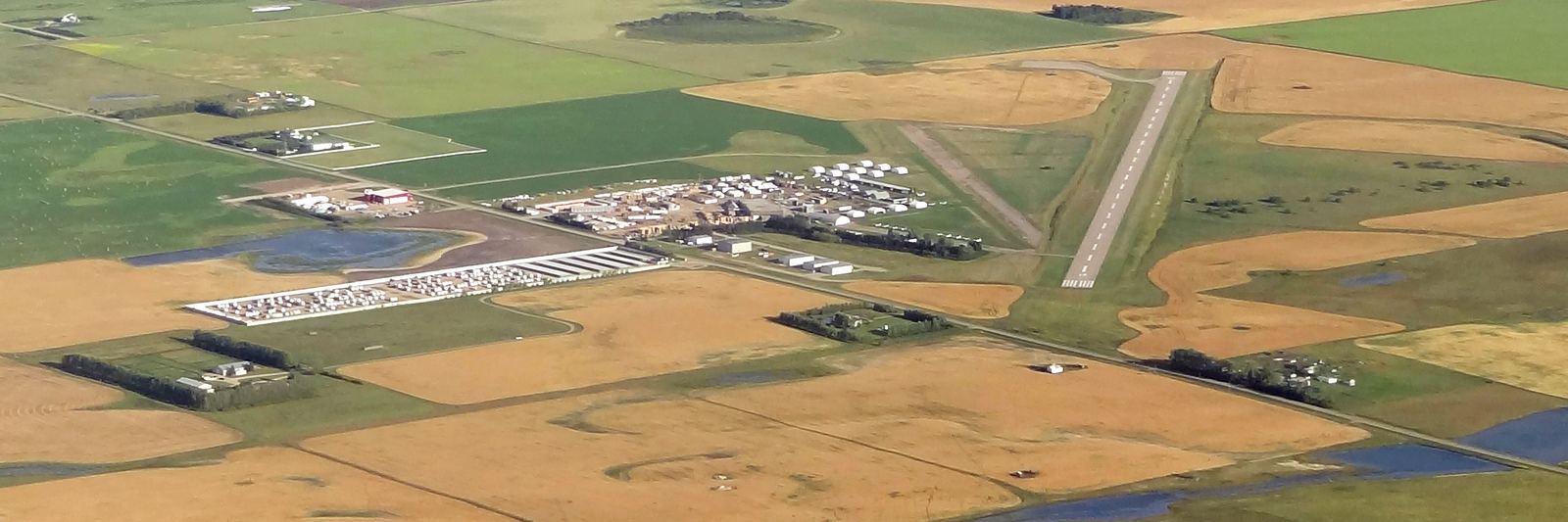 Aerial view of Airdrie Airport's runway and hangars surrounded by farmland