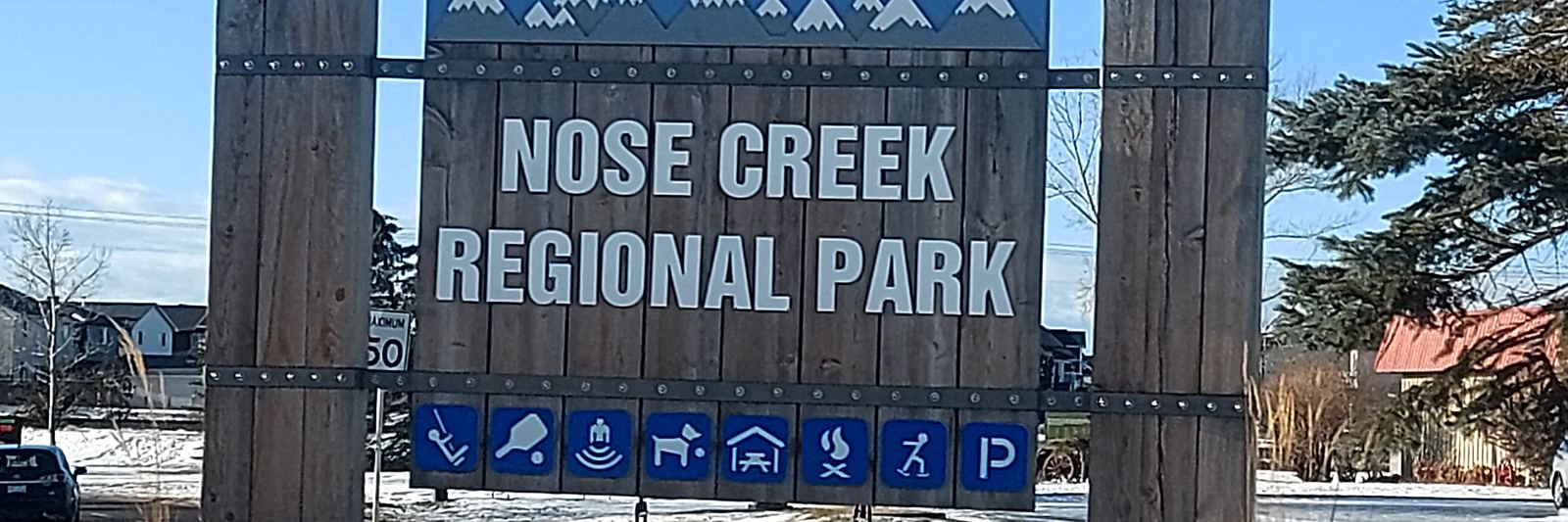Wooden Nose Creek Regional Park sign with park amenity icons in Airdrie, Alberta, in winter